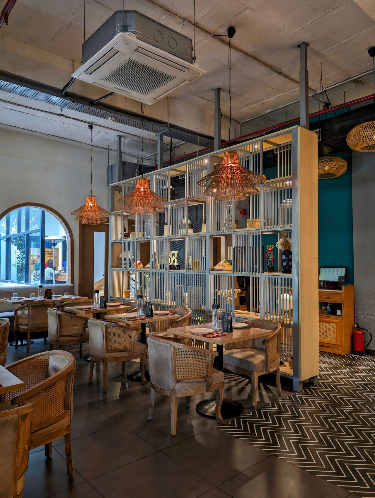 A restaurant dining room before service: cane chairs, set tables and a POS terminal on the counter