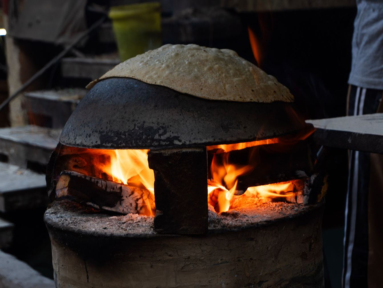 A roti puffing on the dome of a tandoor over glowing coals and open flame